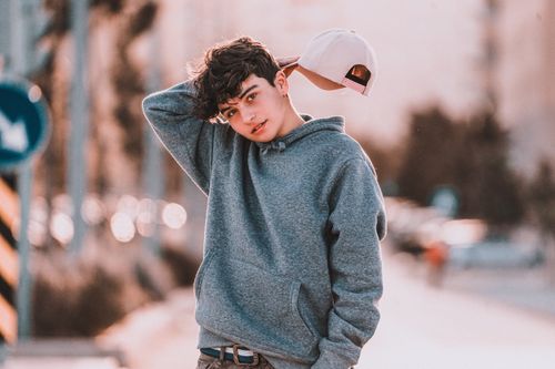 Free Contemplative teenager in stylish apparel with raised arm standing with tilted head on street while looking at camera Stock Photo