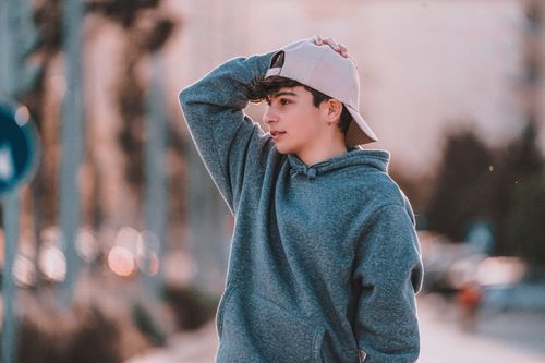 Free Contemplative male adolescent in stylish clothes with cap looking away in town in daytime Stock Photo