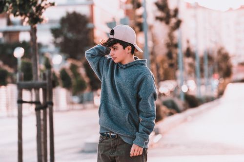 Free Pondering male teen in stylish wear touching cap on pavement in town while looking away Stock Photo