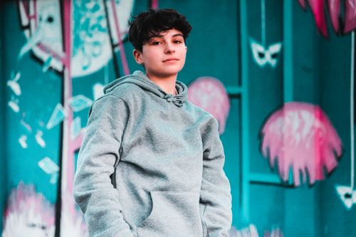 Free From below of charming male teenager in trendy apparel looking at camera near metal wall with graffiti Stock Photo