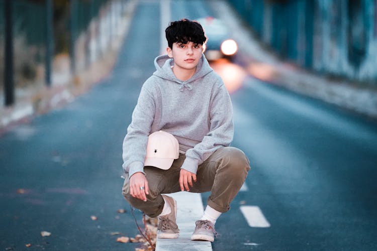 Stylish Male Teen With Cap On Barrier Between Roads