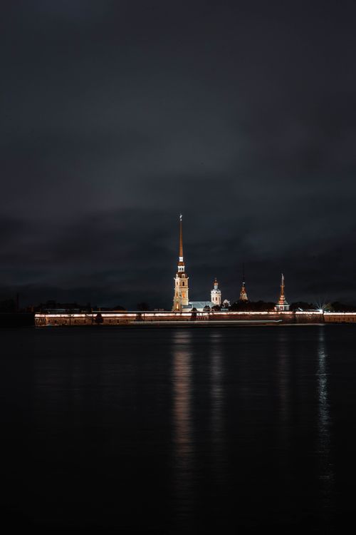 Free A serene view of a tall illuminated tower reflecting on calm water against a dark night sky. Stock Photo