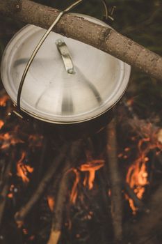 Close-up view of a metal pot hanging over a campfire for outdoor cooking.