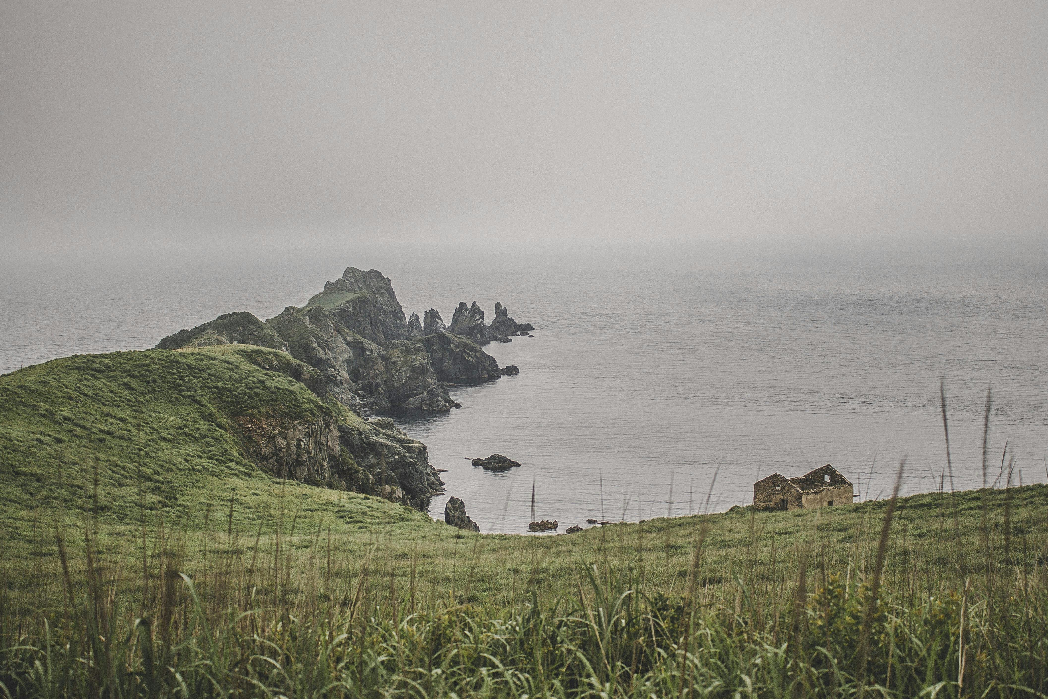 雾气缭绕的沿海景观，以悬崖和海边废弃的小屋为特色