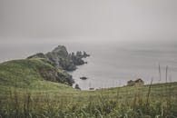 雾气缭绕的沿海景观，以悬崖和海边废弃的小屋为特色