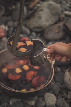 Close-up of fruit being ladled in a metal cup over a rustic outdoor setting.
