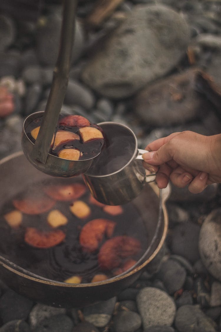 Hand Holding Stainless Cup With Soup Ladle On Top 