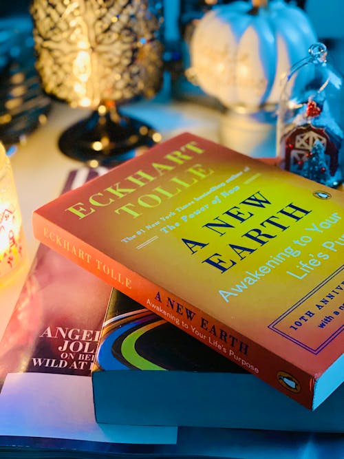 Free High angle composition of stacked books in softcover placed on bedside table near decorative souvenirs and candleholders with burning tealight in evening Stock Photo