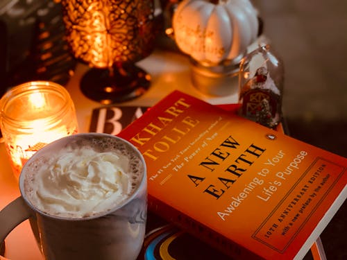 From above stack of modern literature books placed on bedside table near mug with glace coffee and burning tealight in candleholder