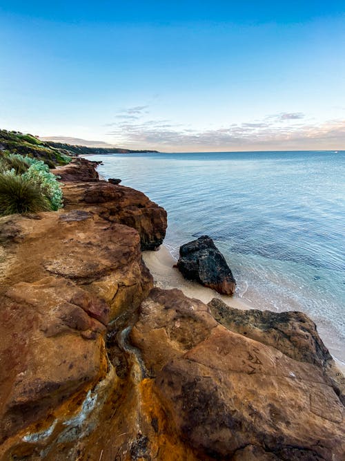 Spectacular view of rough mossy shore washed by tranquil turquoise ocean on clear day