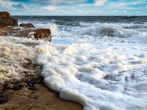 Scenic view of foamy ocean waves rolling on rough rocky coast against clear blue sky