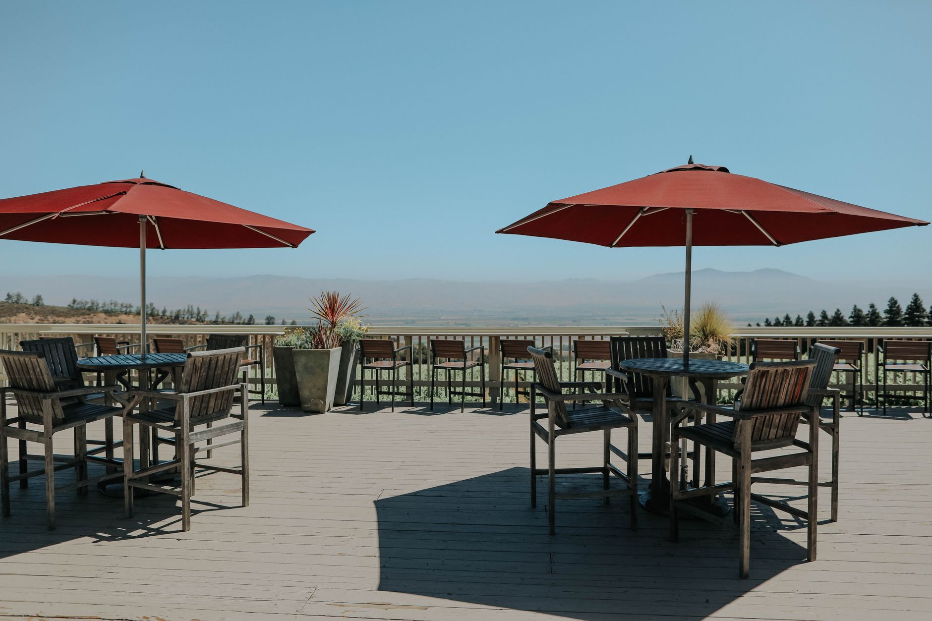 Elegant outdoor terrace with red umbrellas and wooden furniture under a clear blue sky.