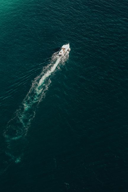 Aerial shot of a boat making waves as it cruises through the vast open sea.