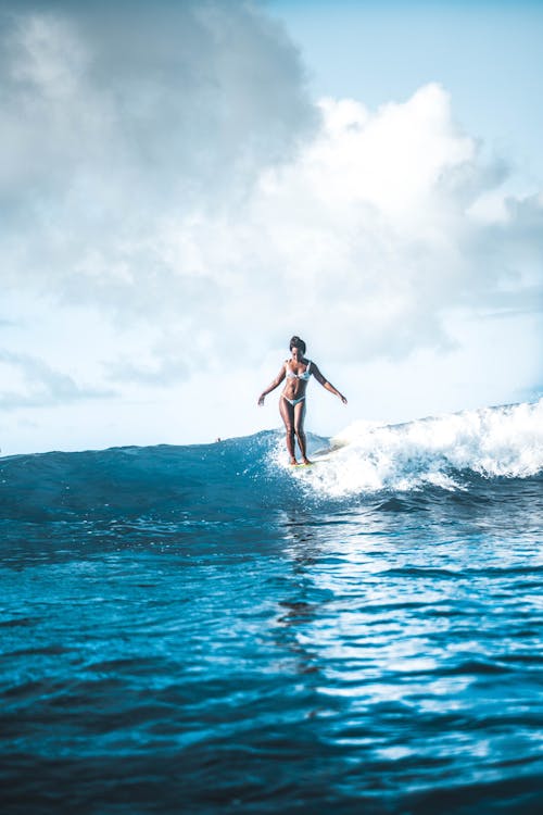 Full body graceful female surfer in white swimsuit splashing seawater while practicing in surfing on clear sunny day