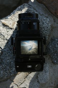 Close-up of a camera screen showing a mountain landscape, set on rocky terrain.