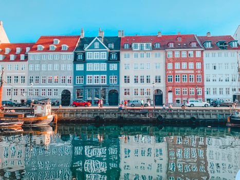 Amazing scenery of typical aged colorful residential buildings located on canal with moored boats against cloudless blue sky in Copenhagen