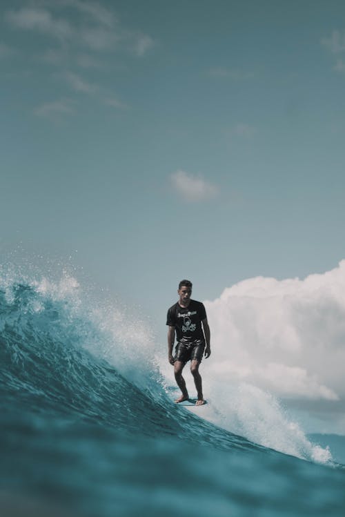 Full body of young determined male athlete doing trick on surfboard while riding splashing waves on sunny day