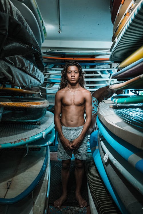 Young ethnic man standing among surfboards