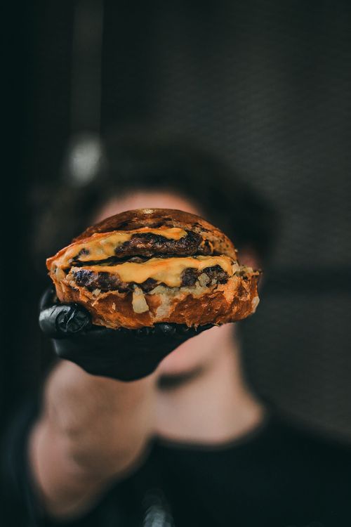 Free Mouth-watering cheeseburger with a juicy beef patty held by a gloved hand, perfect for food enthusiasts. Stock Photo