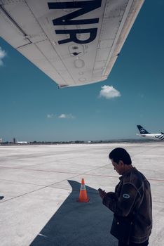 Side view of adult ethnic male airport worker standing on airfield near plane against blue sky