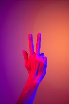 A hand making a peace gesture in vibrant neon lighting, ideal for creative and abstract stock imagery. by cottonbro studio