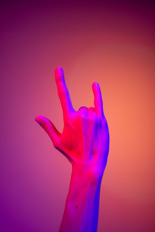 Free A hand making the ILY sign, illuminated by vibrant neon lights against an orange background. Stock Photo