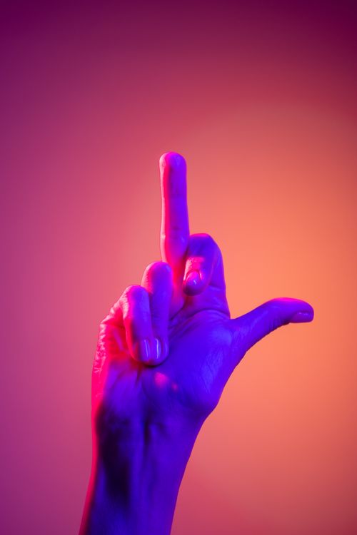 Free A creative neon-lit hand showing a gesture against a colorful background, perfect for expressive communication themes. Stock Photo