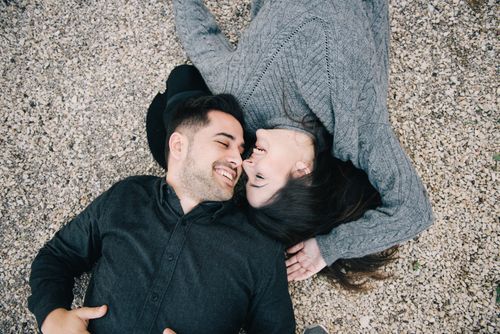 Free A joyful couple lying side by side on a pebbled surface, smiling affectionately at each other. Stock Photo