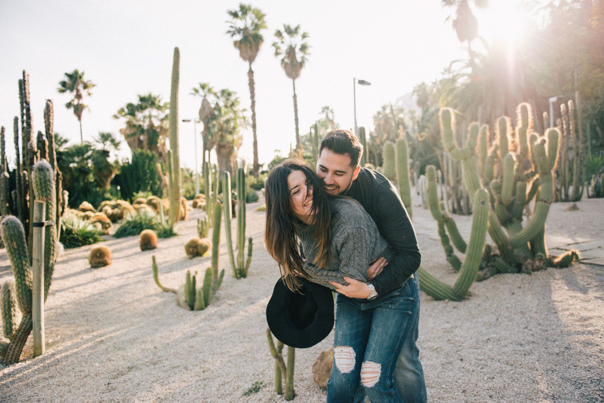 Happy couple embracing in a sunny desert garden filled with cacti and palm trees.