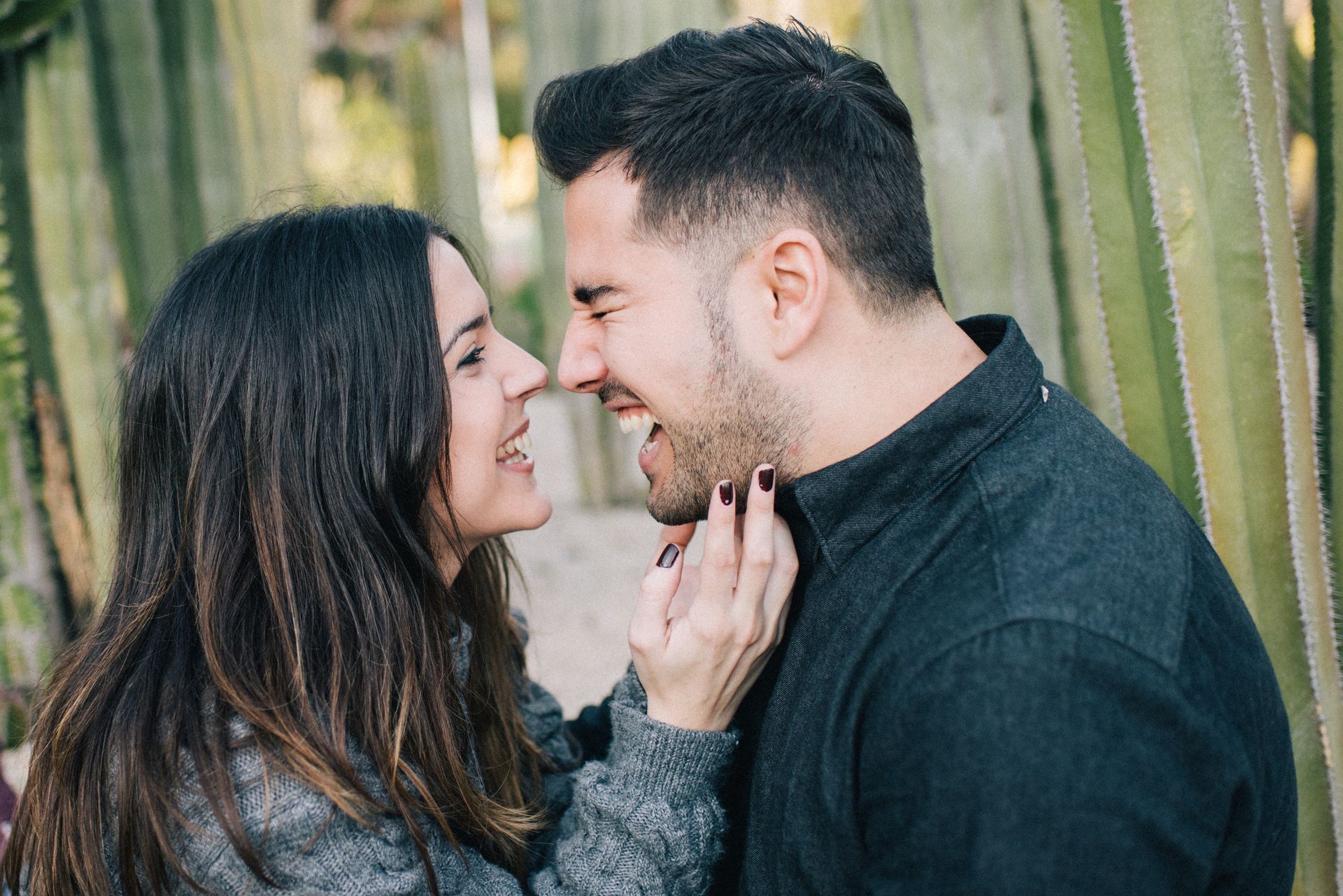 A happy couple laughing face to face in an outdoor setting with cactuses around.