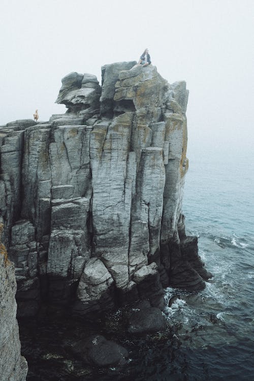 Person Sitting on Rock Formation Near Sea