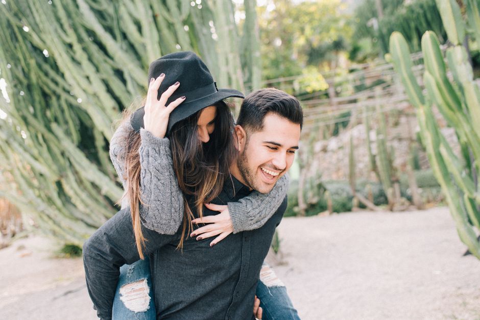 Happy couple enjoying a playful piggyback ride surrounded by lush cacti outdoors.