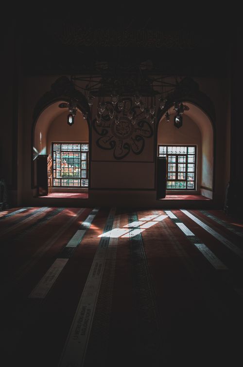 Free Interior of empty prayer room in aged mosque with arched windows and chandelier in sunlight Stock Photo