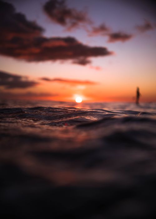 Free A tranquil ocean view at sunset with a silhouette of a surfer, perfect for creating a calming atmosphere. Stock Photo