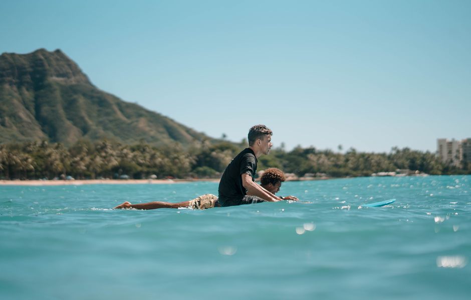 Two surfers paddling their boards near Diamond Head, enjoying the Hawaiian sun and waves.