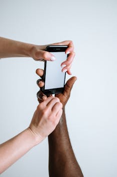 Close-up of diverse hands holding a smartphone with a blank screen.
