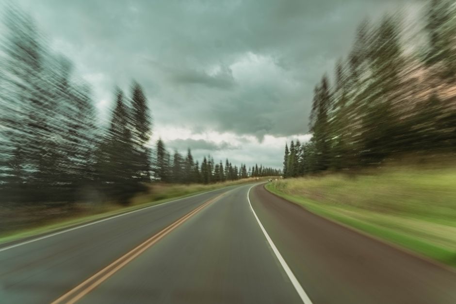 Blurred motion of a winding forest road under cloudy skies captured at dawn.