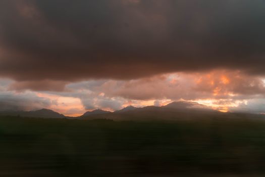 A serene sunset with dramatic clouds over mountain silhouettes.