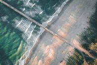 从空中俯瞰，宁静的海滩上，海浪拍打着海岸，码头向海洋延伸
