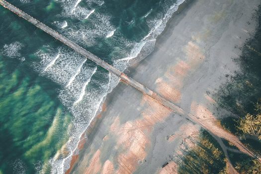 从空中俯瞰，宁静的海滩上，海浪拍打着海岸，码头向海洋延伸