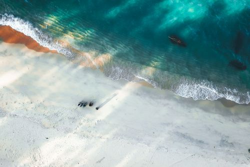 Free Stunning drone shot capturing a calm and serene beach with gentle ocean waves lapping the shore. Perfect for nature and travel imagery. Stock Photo