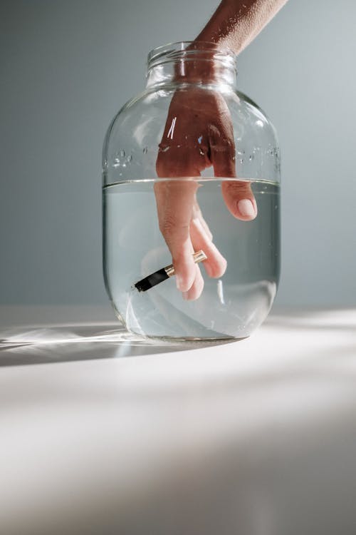 Photo Of Person's Hand Submerged On A Jar With Water