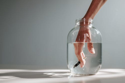 Photo Of Person's Hand Submerged On A Jar With Water