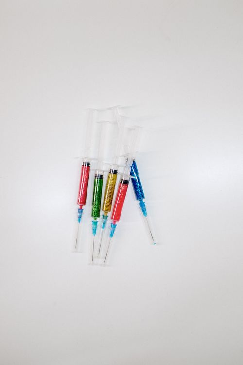 Free A set of vibrant glitter-filled syringes arranged on a plain white surface. Stock Photo