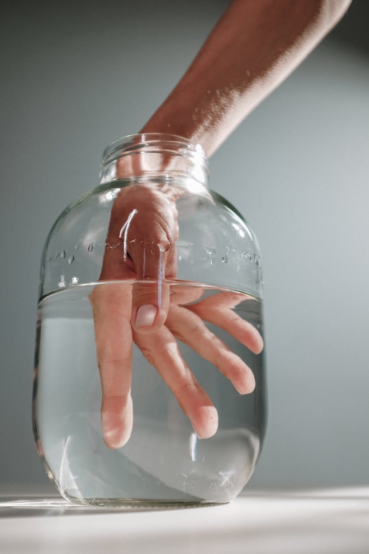 Photo Of Person's Hand Submerged On A Jar With Water