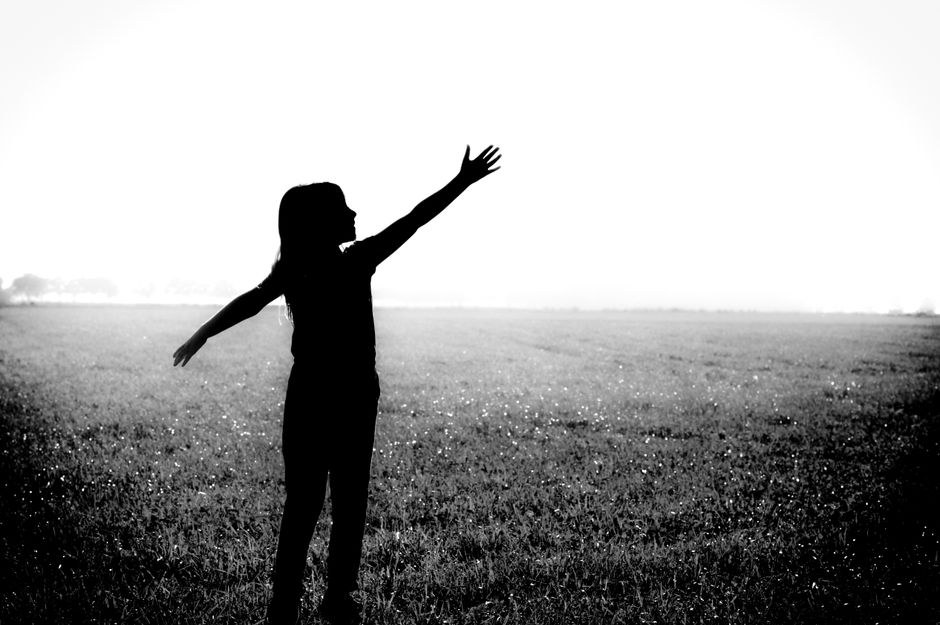 Black and white silhouette of a woman with arms outstretched in a field, symbolizing freedom and joy.