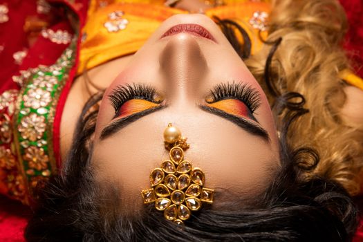 Close-up of a woman with colorful traditional bridal makeup and ornate jewelry.