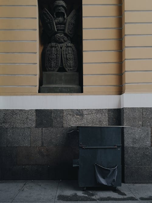 Trash can placed near wall of Triumphal Arch of General Staff Building in Saint Petersburg with architectural element in niche