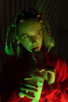 A young woman sips a beverage under vibrant neon lighting, creating a stylish and edgy look.