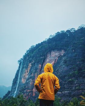 在印度尼西亚苏门答腊岛，一位穿着黄色夹克的孤独冒险家正在观察瀑布